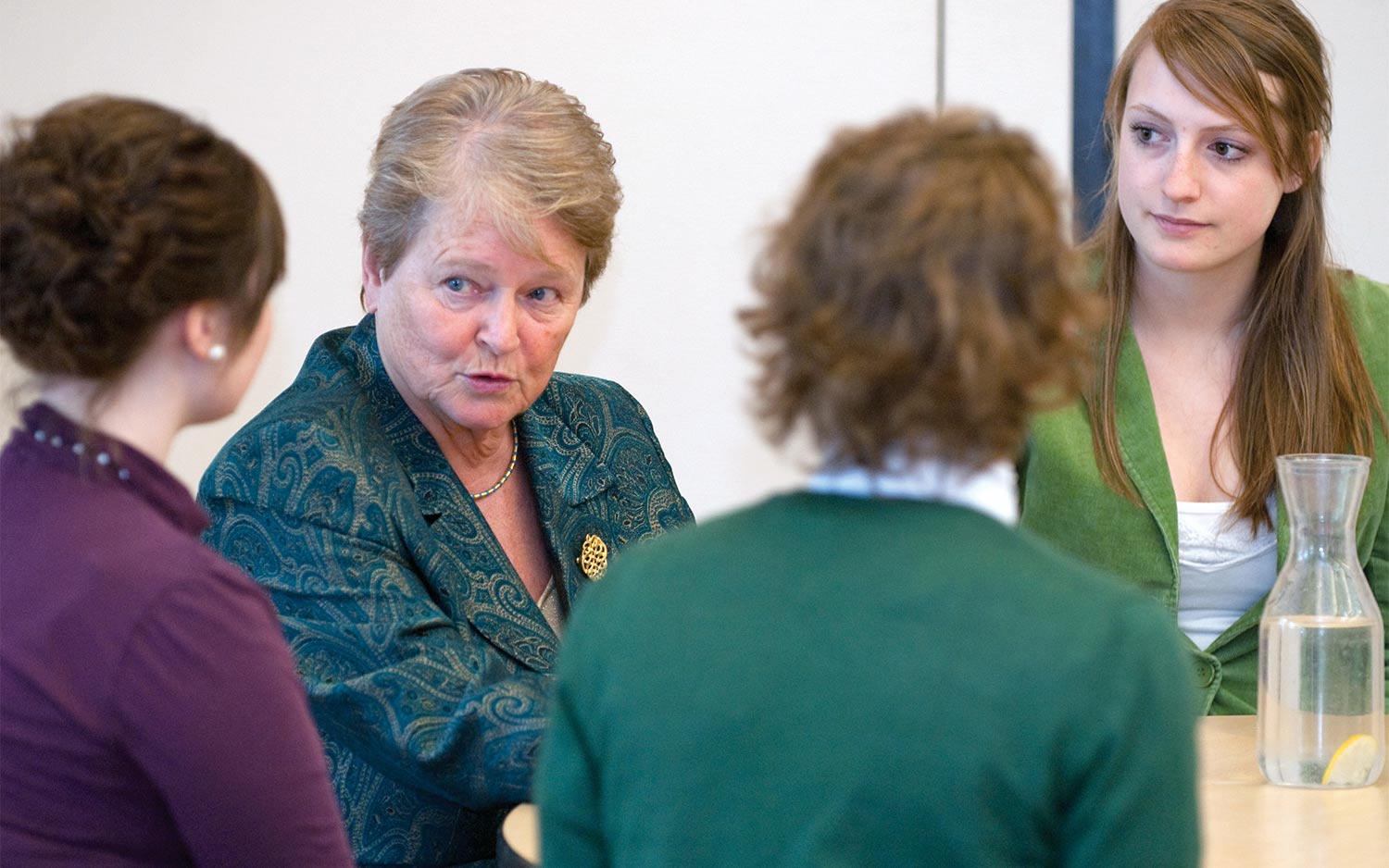 A professional older woman speaking with younger women at a table